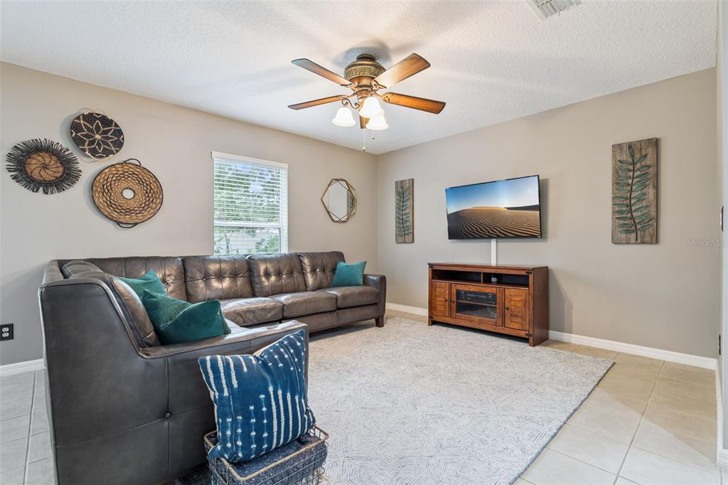 A living room features a dark leather sectional, a television on a wooden console, and decor — 657 PREAKNESS CIRCLE, DELAND, FL