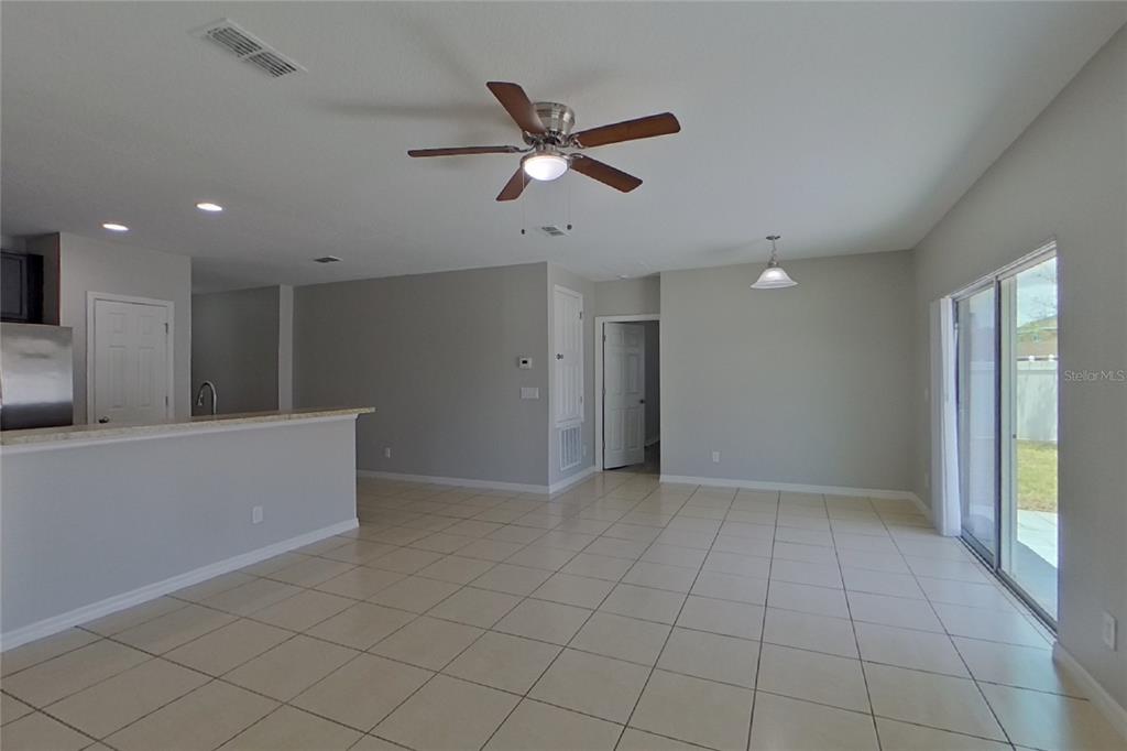 An open-concept living area features light tile flooring, a ceiling fan, and sliding glass doors — 2800 GLENDIVE DRIVE, KISSIMMEE, FL