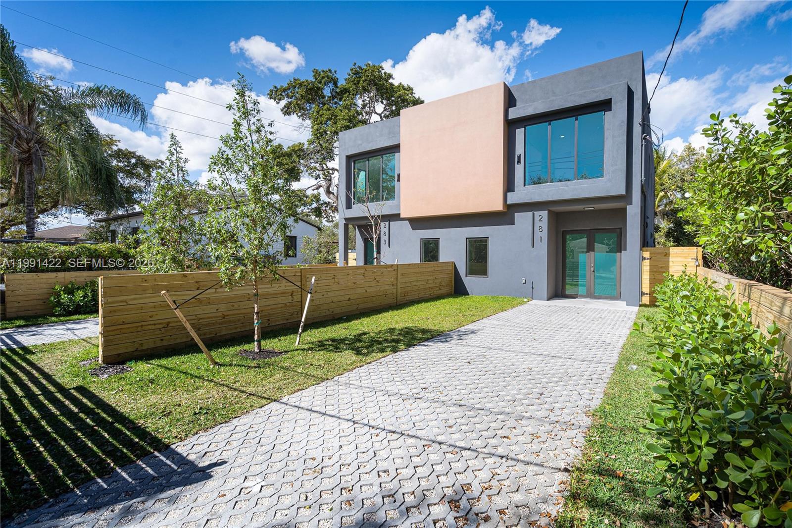 A modern two-story duplex with a paved driveway and wooden fencing under a blue sky — 283 NW 52 St # 283, Miami FL 33127, MIAMI, FL