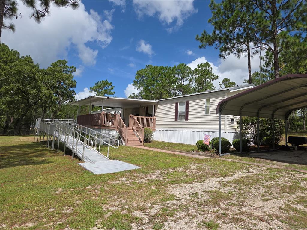 A manufactured home features a wooden deck with a wheelchair ramp and a metal carport — 750 NE 131ST TERRACE, WILLISTON, FL