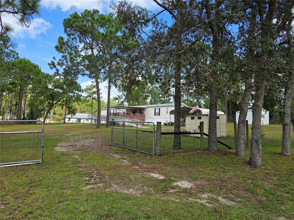 A mobile home with a wheelchair ramp sits on a grassy lot behind a wire fence — 750 NE 131ST TERRACE, WILLISTON, FL