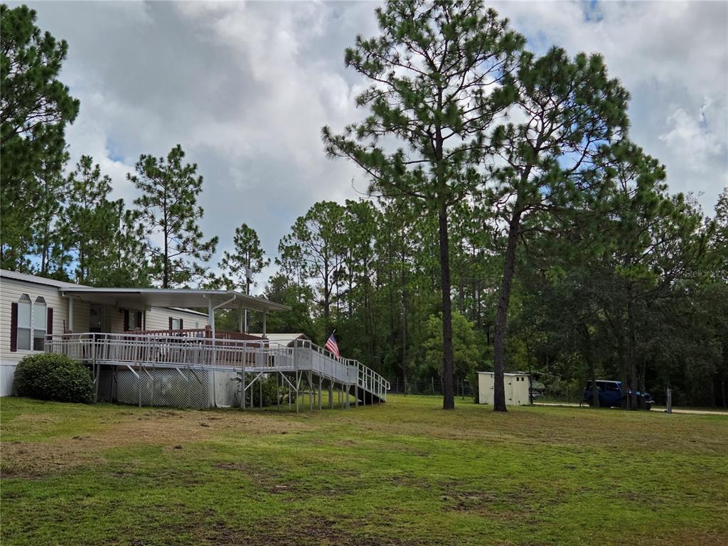 A mobile home with a large elevated deck and wheelchair ramp sits on a grassy lot — 750 NE 131ST TERRACE, WILLISTON, FL