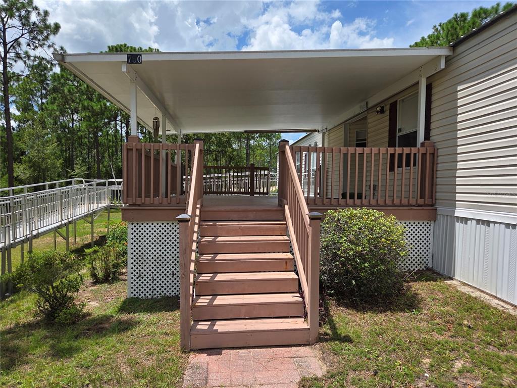 A mobile home exterior features a covered wooden deck with stairs and an accessibility ramp — 750 NE 131ST TERRACE, WILLISTON, FL
