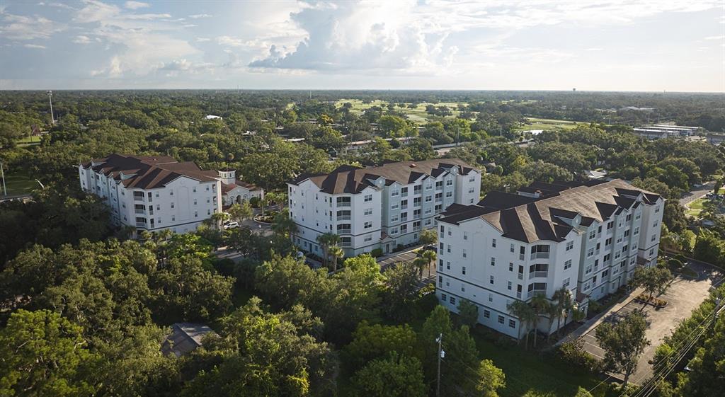 An aerial view shows three multi-story apartment buildings surrounded by dense trees and greenery — 4 MAGGIE LANE UNIT Symphony, SARASOTA, FL