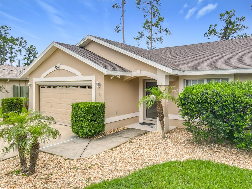 A tan single-story house features a garage, a front entryway, and landscaped bushes — 8 BAINBRIDGE LANE, PALM COAST, FL