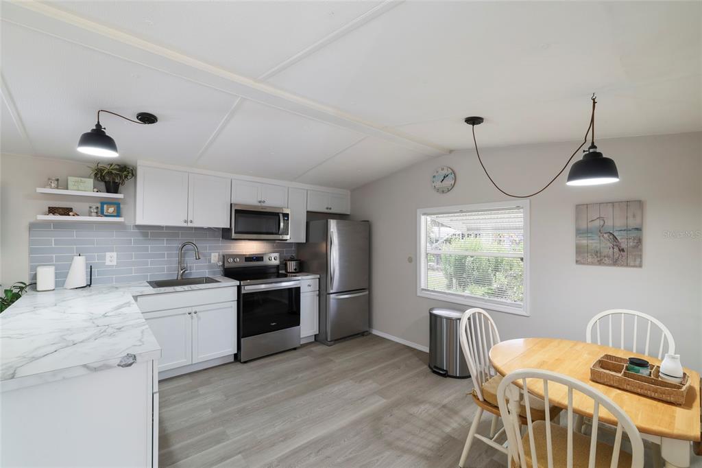 A kitchen and dining area with white cabinets, stainless steel appliances, and light wood flooring — 3119 SUNNY HARBOR DRIVE, PUNTA GORDA, FL