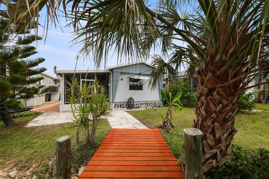 A wooden walkway leads to a mobile home with a screened porch and palm trees — 3119 SUNNY HARBOR DRIVE, PUNTA GORDA, FL