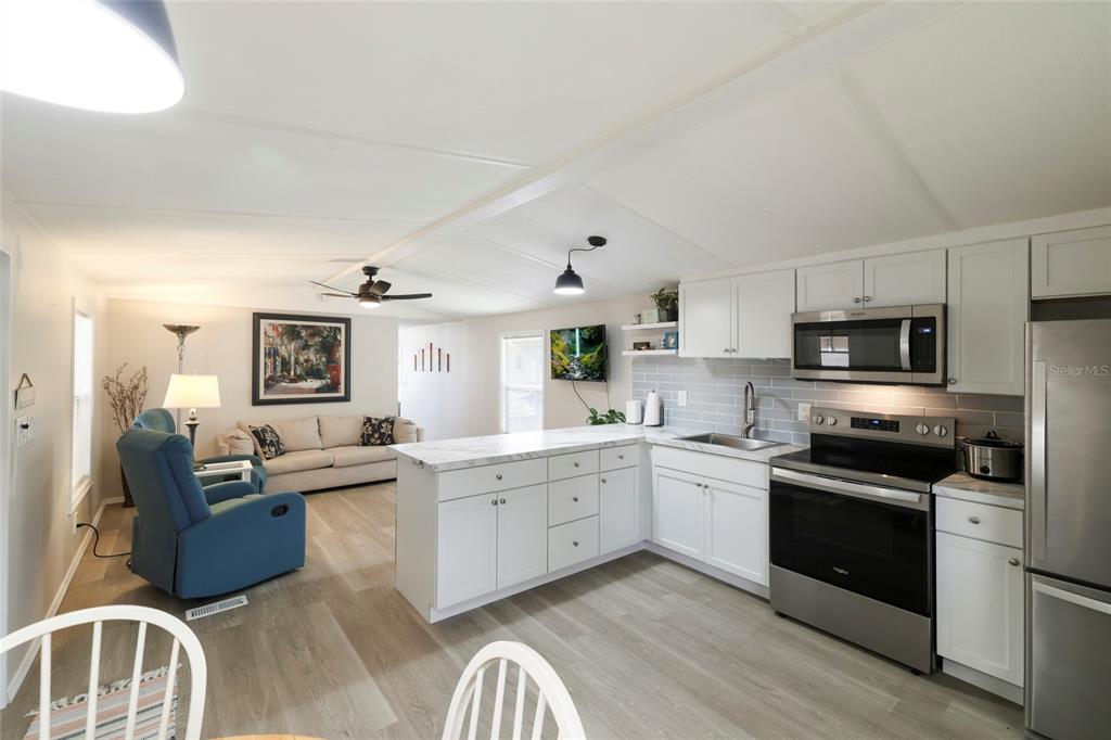 An open-concept kitchen with white cabinets and a marble-look island overlooks a living room — 3119 SUNNY HARBOR DRIVE, PUNTA GORDA, FL
