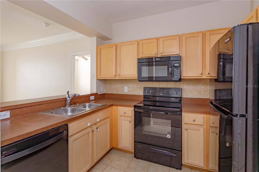 A kitchen features light wood cabinets, black appliances, a double sink, and tan tile backsplash — 12849 MADISON POINT CIRCLE UNIT 201, ORLANDO, FL