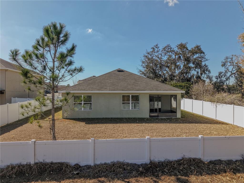 The rear exterior of a single-story house with a fenced yard and a screened porch — 5618 GEIGER ESTATES DRIVE, ZEPHYRHILLS, FL