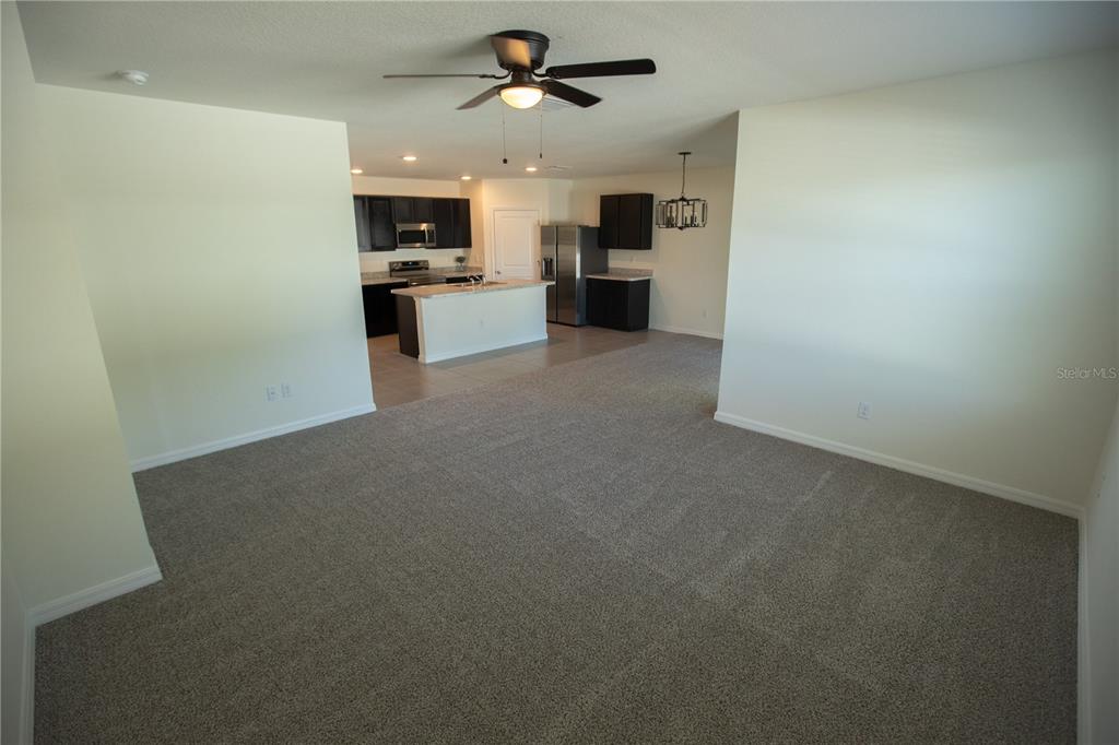 A carpeted living area opens into a kitchen with dark cabinets and a breakfast bar — 5618 GEIGER ESTATES DRIVE, ZEPHYRHILLS, FL
