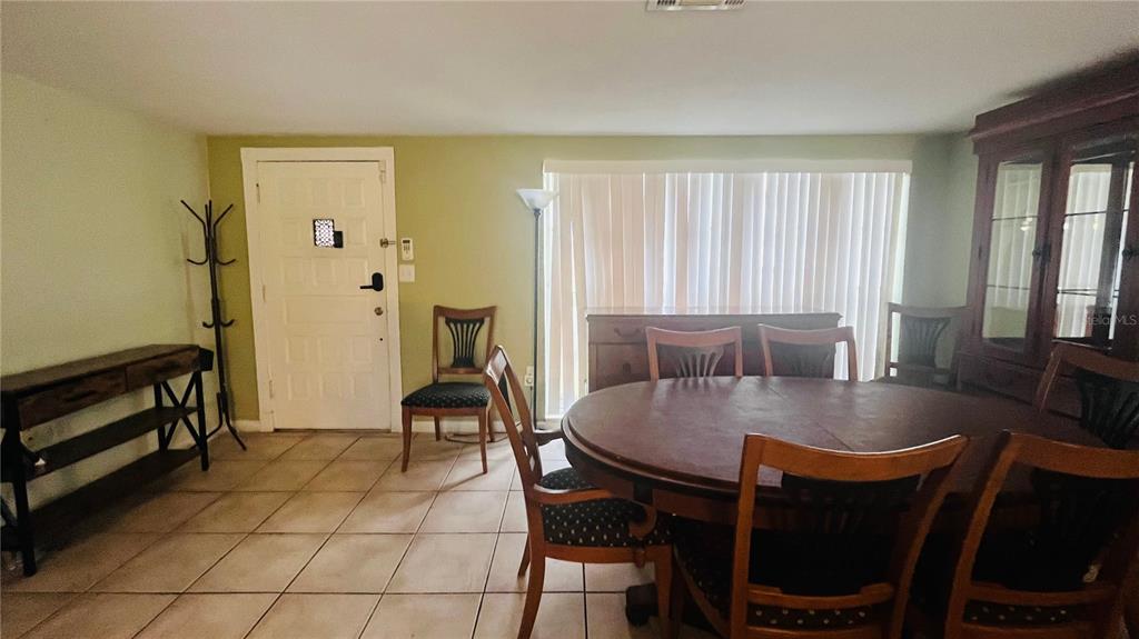 A dining room features a round wooden table, matching chairs, tile flooring, and a white door — 7310 BRENTWOOD DRIVE, PORT RICHEY, FL