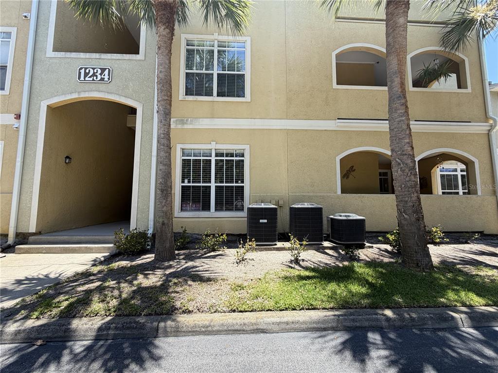 The exterior of a multi-story apartment building features beige stucco walls, arched balconies, and air-conditioning units — 1234 S MISSOURI AVENUE UNIT 316, CLEARWATER, FL