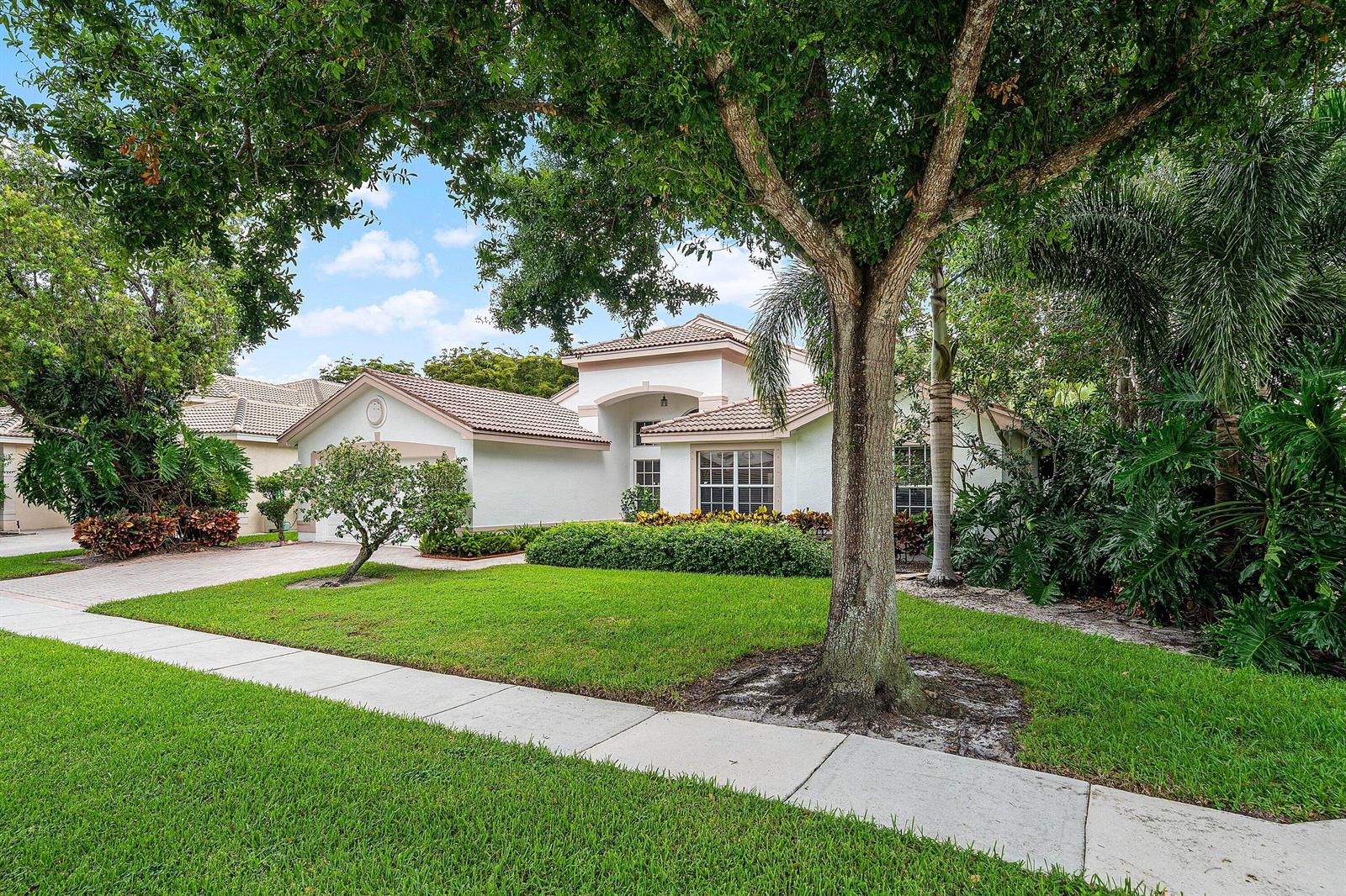 A single-story white house with a tiled roof sits behind a large tree and lawn — 11631 Puerto Boulevard, Boynton Beach FL 33437, BOYNTON BEACH, FL