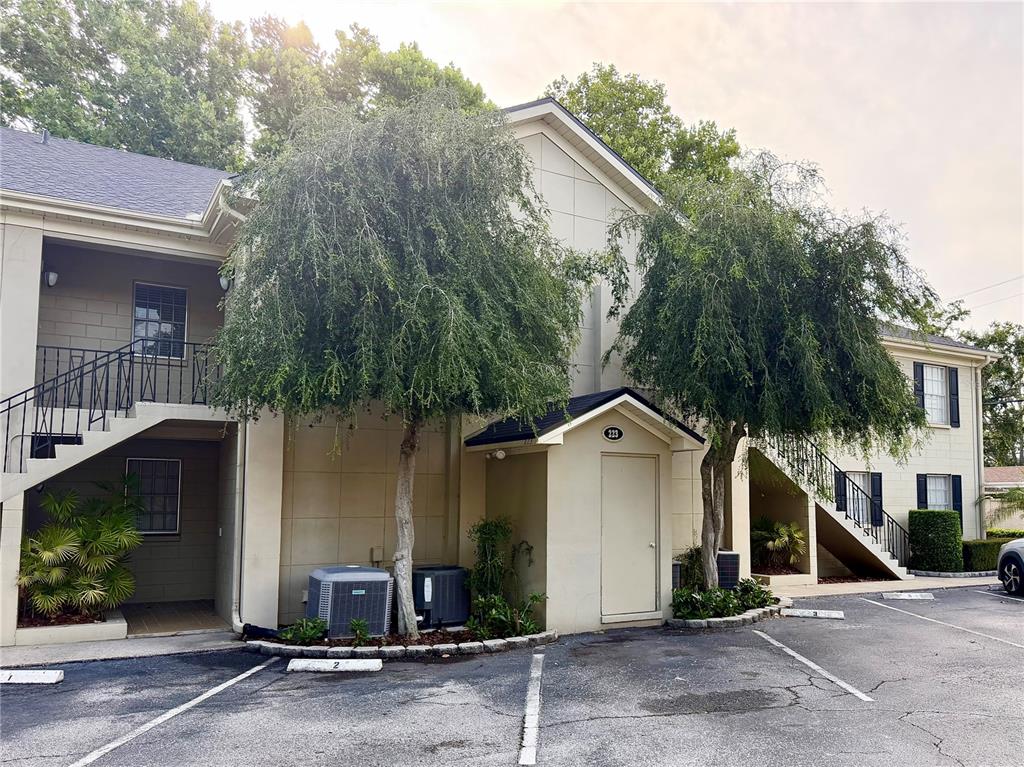 The exterior of a two-story apartment building features beige siding, outdoor staircases, and two trees — 223 WINDSOR STREET UNIT 6, LAKELAND, FL