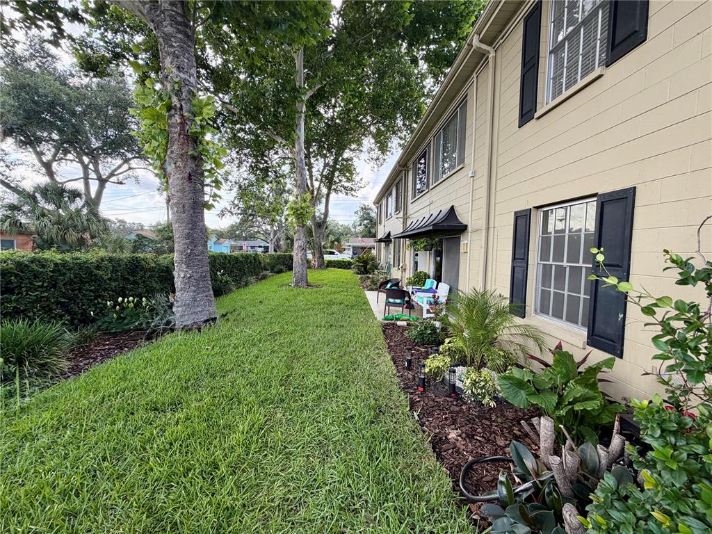 A grassy backyard area sits beside a multi-story building with tan siding and black shutters — 223 WINDSOR STREET UNIT 6, LAKELAND, FL