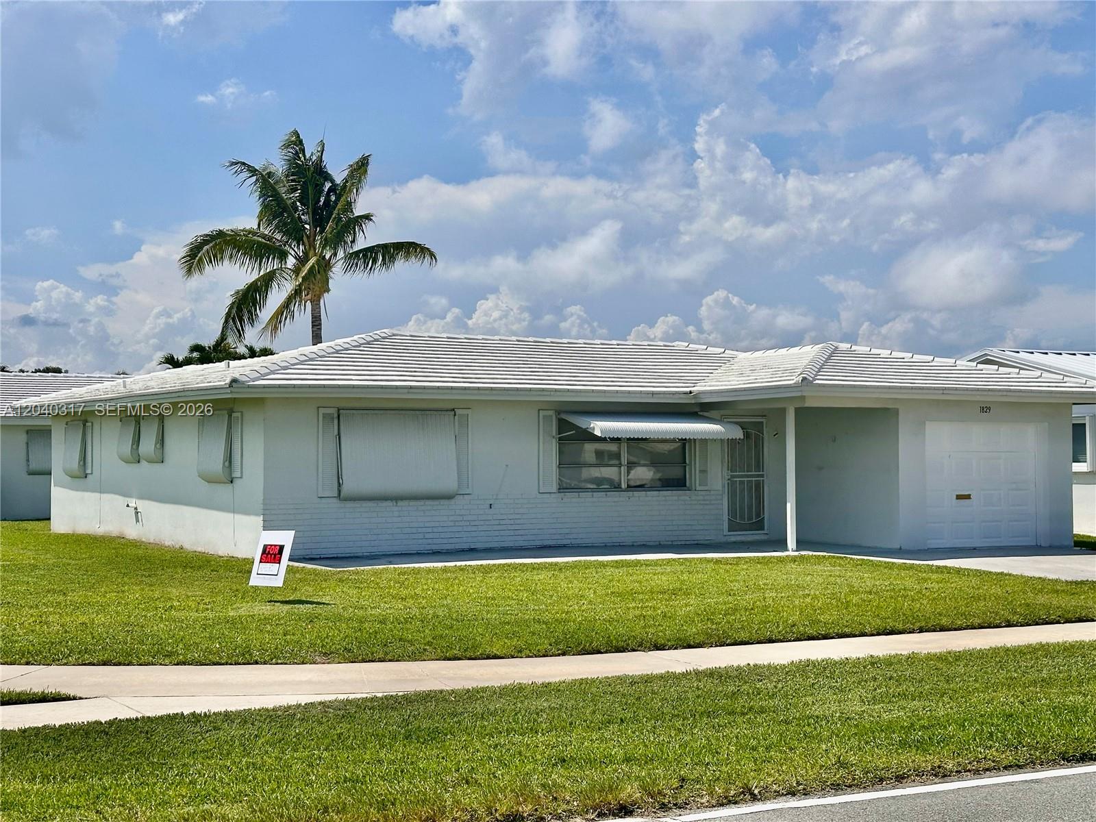A single-story white house with a tiled roof, a palm tree, and a front lawn — BOYNTON BEACH, FL