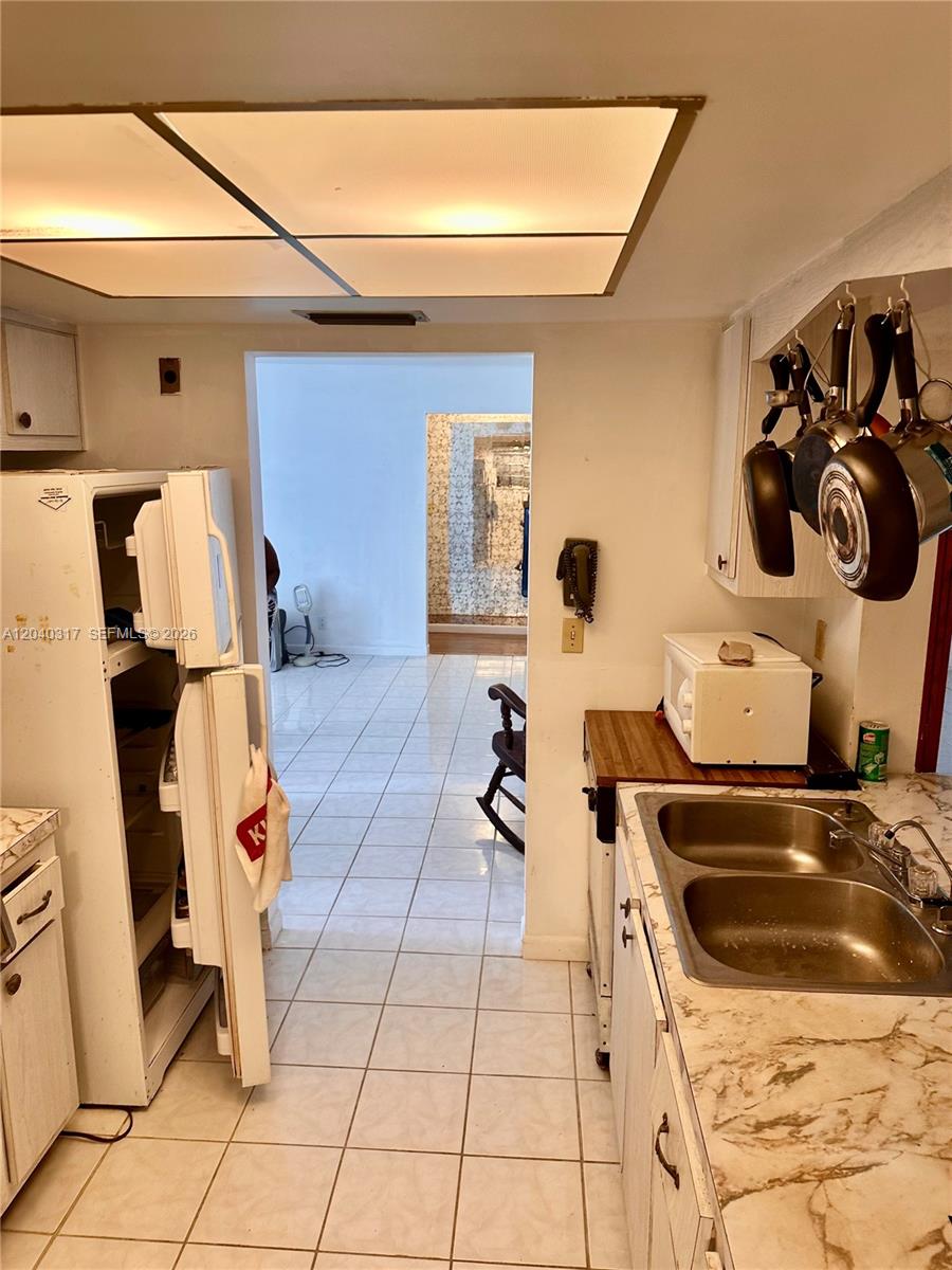 A kitchen with white cabinets, a double sink, and a refrigerator leads to another room — BOYNTON BEACH, FL