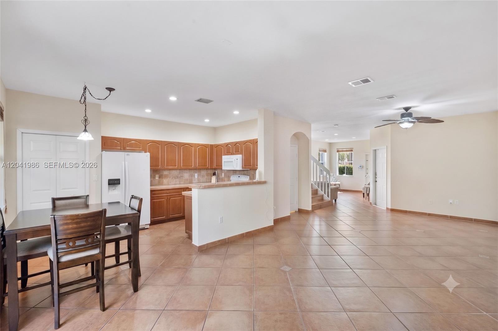 An open-concept kitchen and dining area features wood cabinets, tile flooring, and a ceiling fan — 12334 SW 124th Path, Miami FL 33186, MIAMI, FL