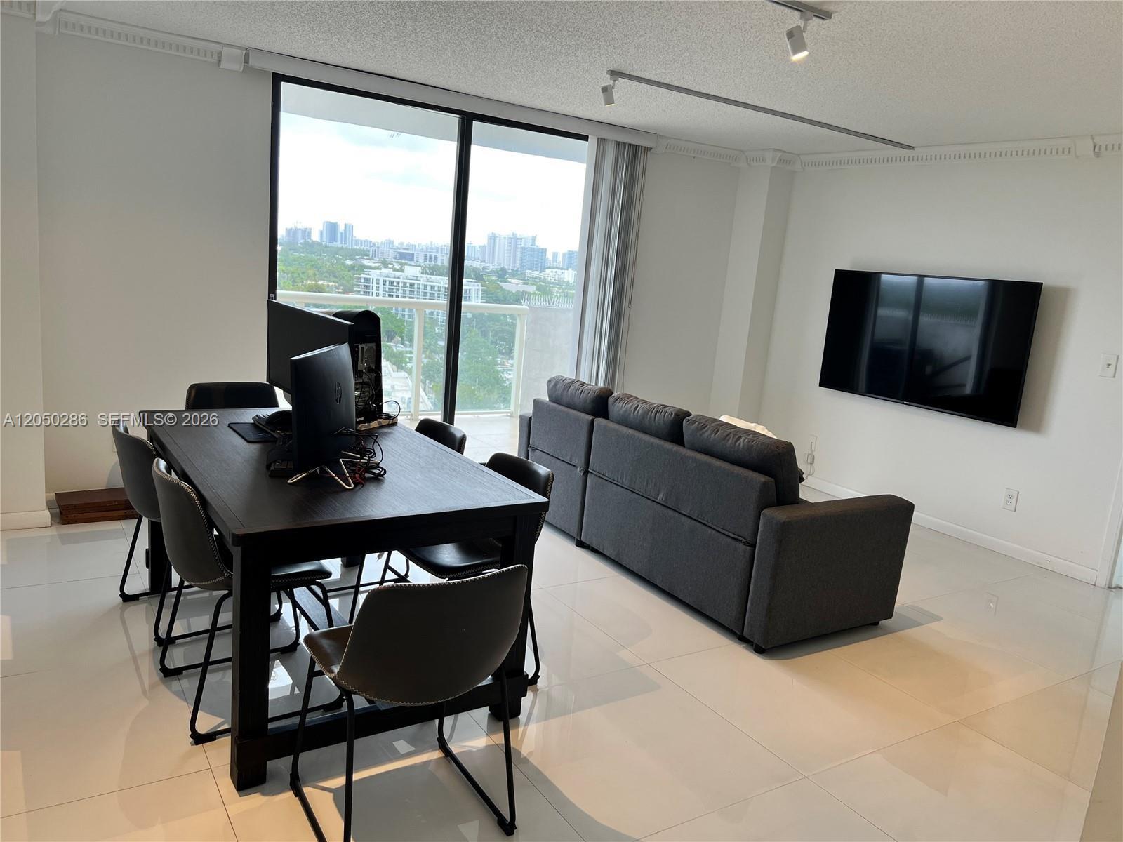 A living and dining area features white tile floors, a dark sofa, and a computer desk — 13499 Biscayne Blvd # 1407, North Miami FL 33181, NORTH MIAMI, FL