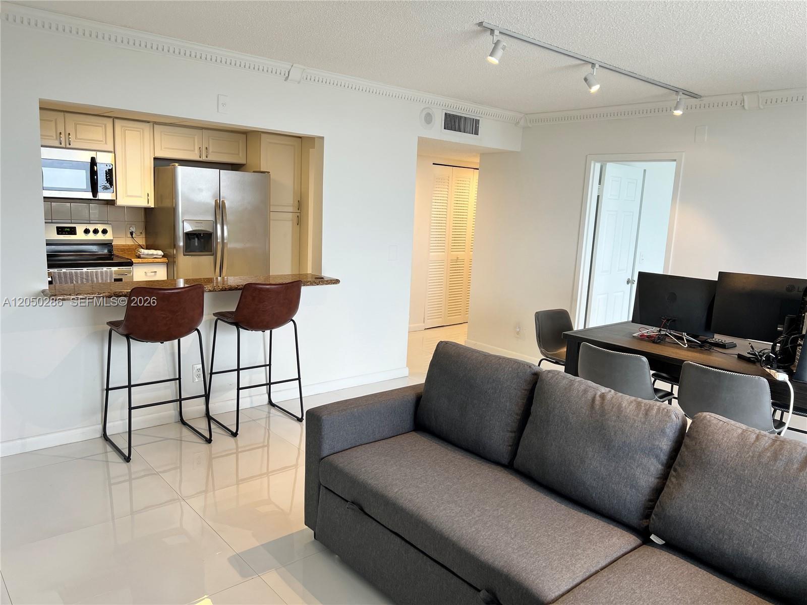 A living room features a grey sofa, a dining area, and an open-concept kitchen — 13499 Biscayne Blvd # 1407, North Miami FL 33181, NORTH MIAMI, FL
