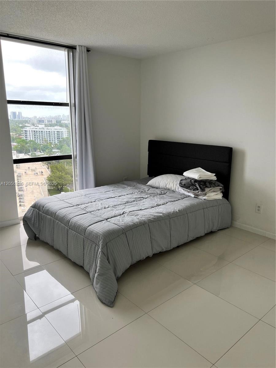 A bedroom features a bed with a grey comforter, a black headboard, and large windows — 13499 Biscayne Blvd # 1407, North Miami FL 33181, NORTH MIAMI, FL