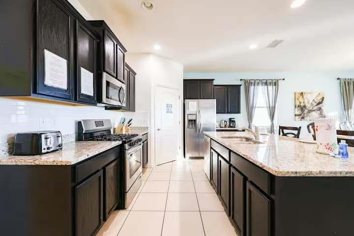 A kitchen features dark wood cabinets, granite countertops, stainless steel appliances, and light tile flooring — 6078 BROAD OAK DRIVE, DAVENPORT, FL