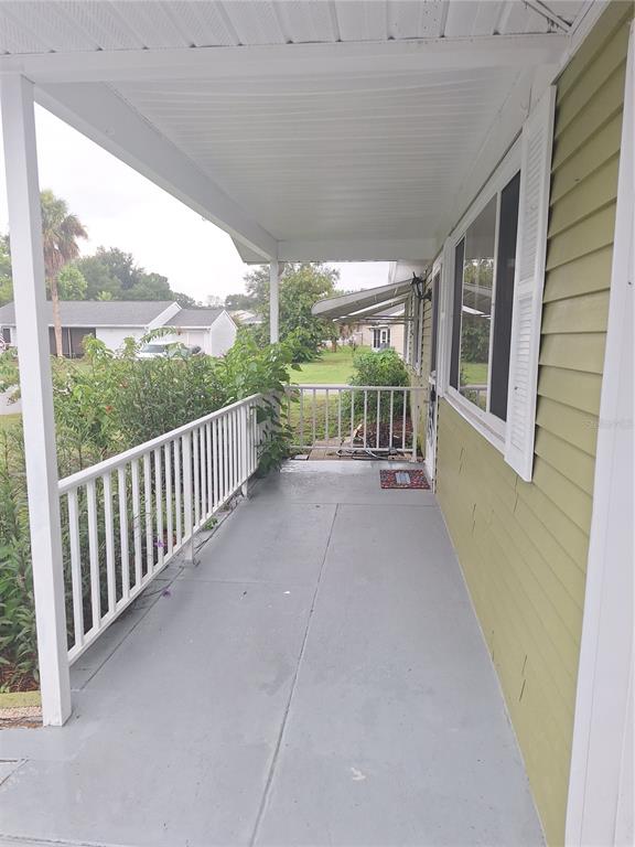 A covered porch with a gray concrete floor, white railings, and light green siding — 8942 SW 109TH LANE, OCALA, FL