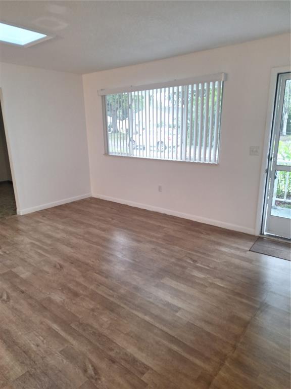 An empty room with light wood-look flooring, white walls, a large window, and a door — 8942 SW 109TH LANE, OCALA, FL