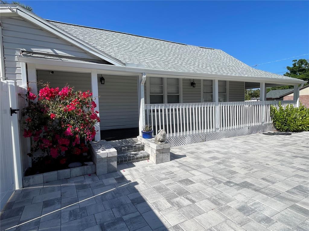 A gray house features a covered front porch with white railings and a paved patio — 7315 S MASCOTTE STREET, TAMPA, FL