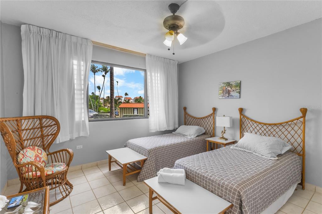 A bedroom features two twin beds with lattice headboards, a wicker chair, and a window view — 227 BEACH VILLAGE UNIT 227, HUMACAO, PR