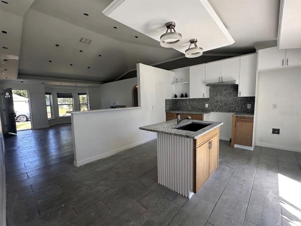 A kitchen with a granite-topped island and white cabinets overlooks an open living area — 1316 BURNLEY COURT, KISSIMMEE, FL