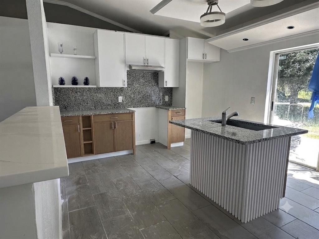 A kitchen features wood lower cabinets, white upper cabinets, granite countertops, and a fluted island — 1316 BURNLEY COURT, KISSIMMEE, FL