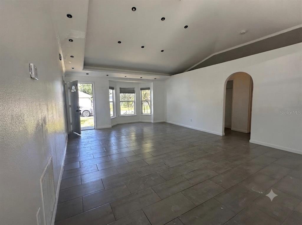 An empty living room features gray tile flooring, a vaulted ceiling with recessed lighting, and windows — 1316 BURNLEY COURT, KISSIMMEE, FL