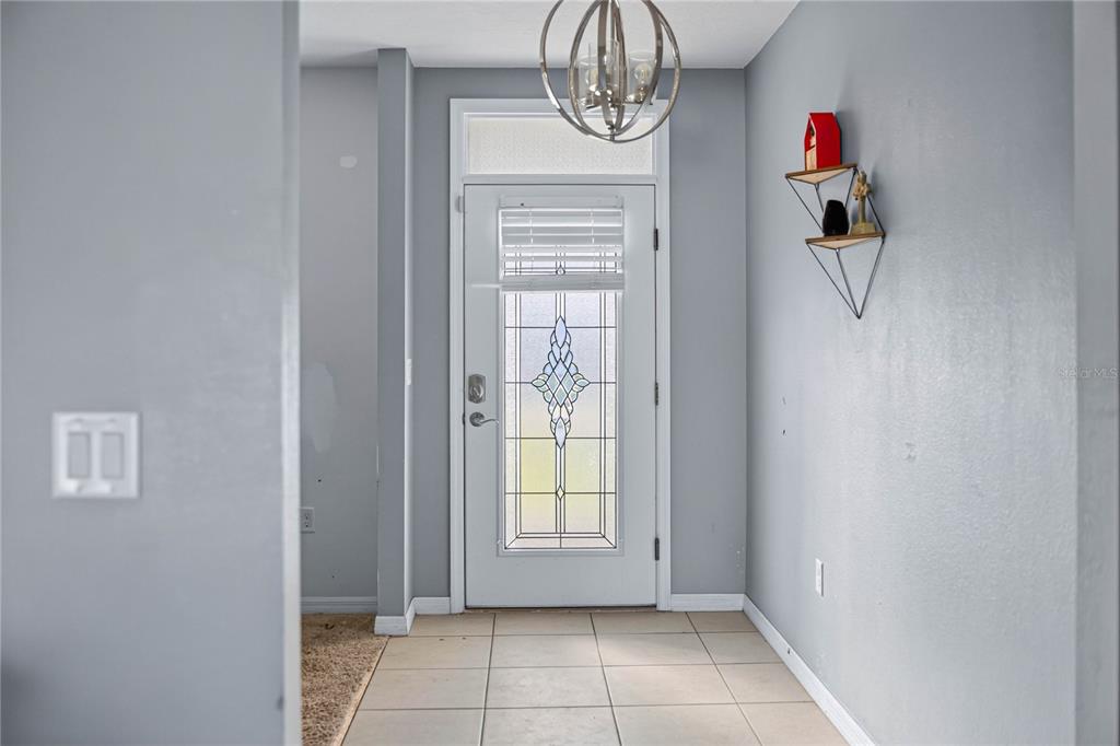An entryway features light gray walls, tiled flooring, a decorative light fixture, and a glass-paneled door — 6022 GREY HERON DRIVE, WINTER HAVEN, FL