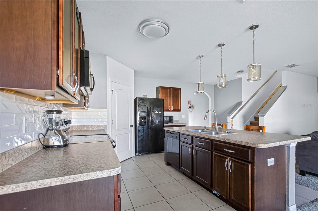 A kitchen features dark wood cabinetry, a central island with a sink, and stainless appliances — 6022 GREY HERON DRIVE, WINTER HAVEN, FL