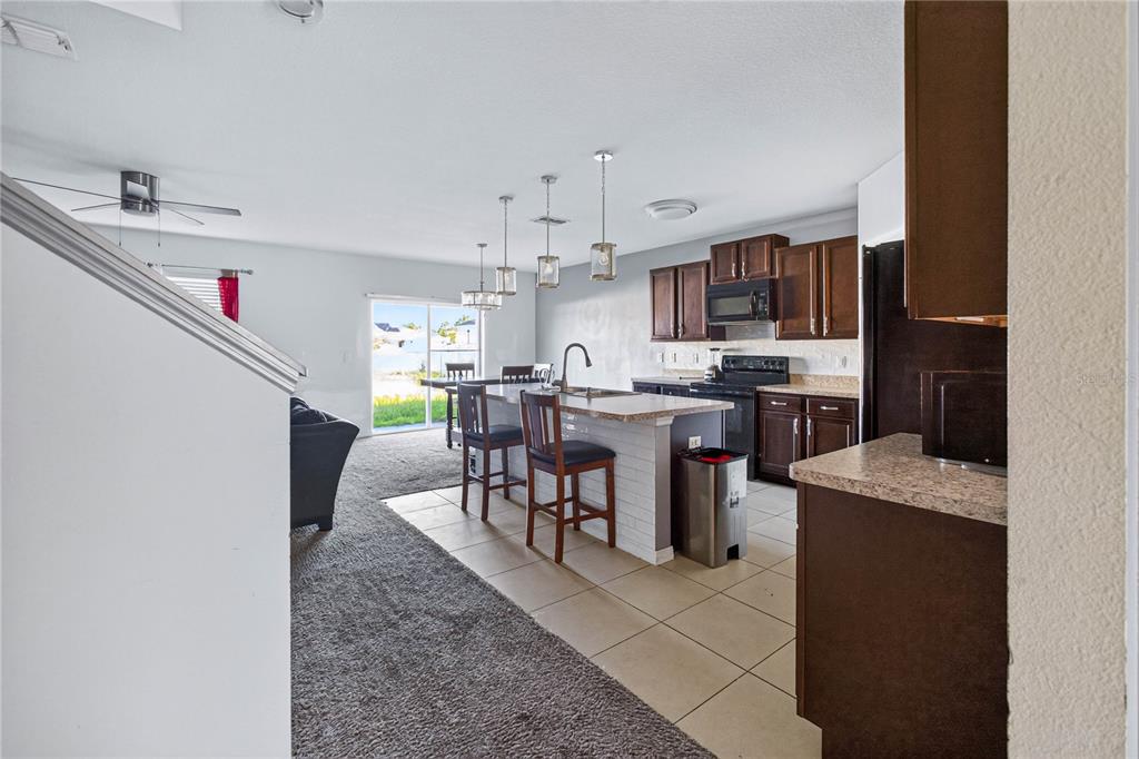 A kitchen with dark wood cabinets and a white brick island overlooks a carpeted living area — 6022 GREY HERON DRIVE, WINTER HAVEN, FL