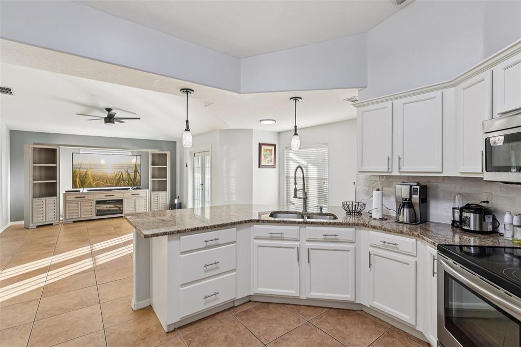 A kitchen with white cabinets and granite countertops overlooks an open-concept living area — 402 OHIO WAY, KISSIMMEE, FL