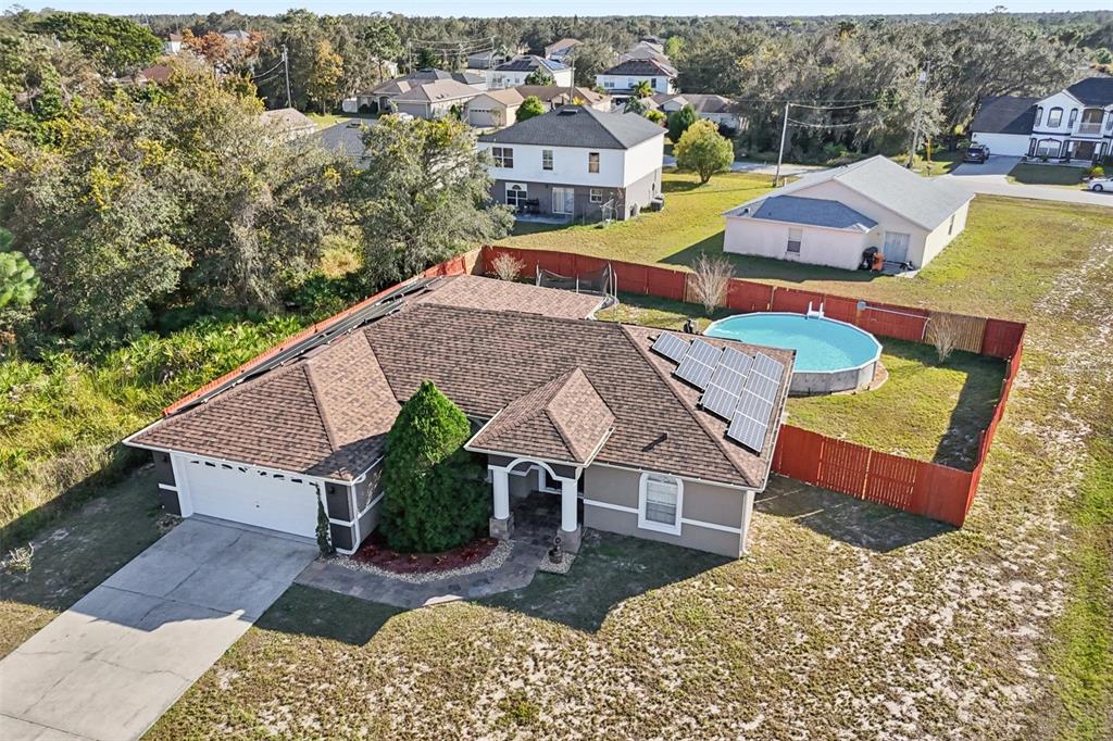 An aerial view of a single-story house with solar panels, a pool, and fenced yard — 402 OHIO WAY, KISSIMMEE, FL