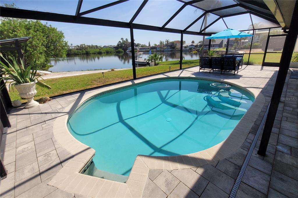 A screened-in pool patio overlooks a canal with a boat docked in the distance — 5717 SEABREEZE DRIVE, PORT RICHEY, FL