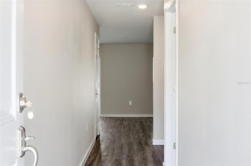A hallway with light-colored walls and wood-look flooring leads toward an open living area — 64 FOXHALL LANE, PALM COAST, FL