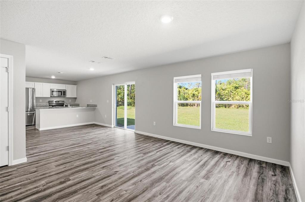 An open-concept living area with gray walls, wood-look flooring, and a kitchen in the background — 64 FOXHALL LANE, PALM COAST, FL