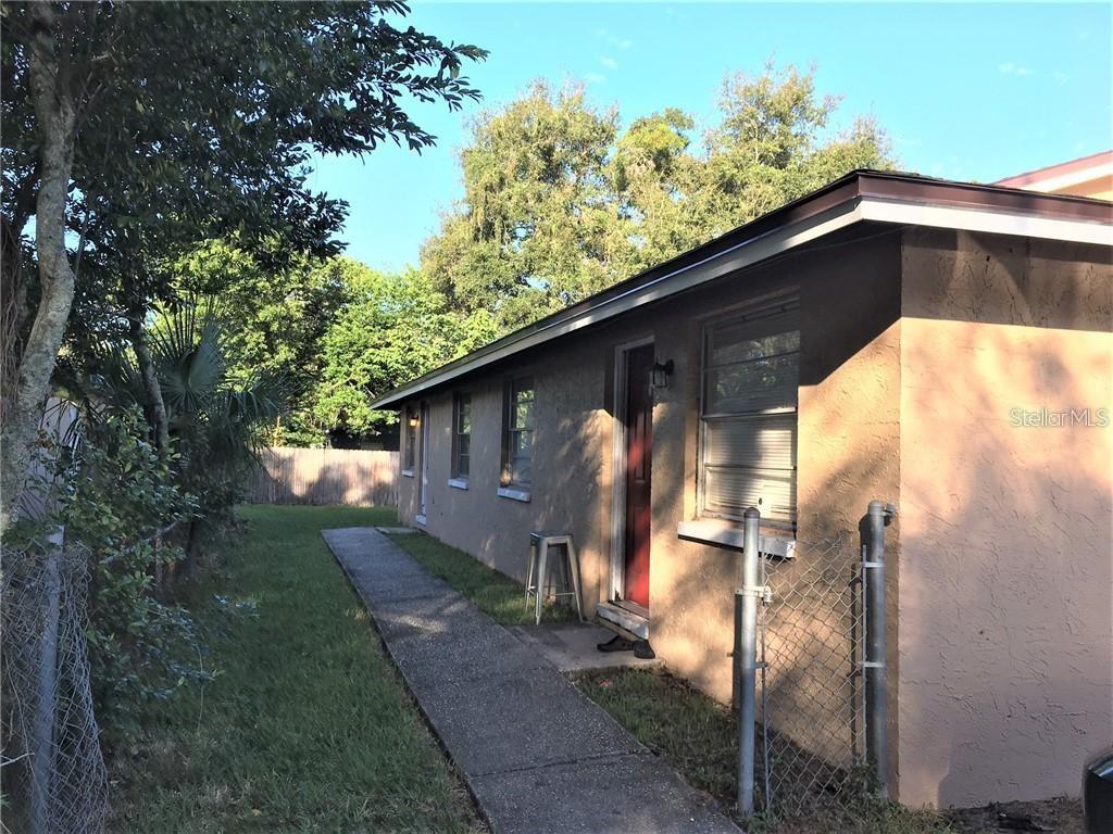 A side view of a tan stucco house with a concrete walkway and chain-link fence — 8306 N 17TH STREET, TAMPA, FL