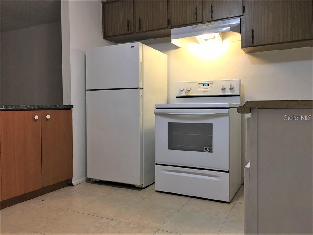 A kitchen features white appliances, wood-toned cabinets, and light-colored tile flooring — 8306 N 17TH STREET, TAMPA, FL