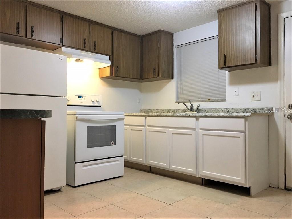 A kitchen features white lower cabinets, wood upper cabinets, white appliances, and granite countertops — 8306 N 17TH STREET, TAMPA, FL