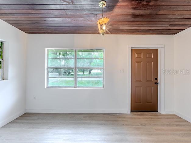 A room with white walls, light wood-look flooring, a wood-plank ceiling, and a brown door — 1440 SE 1ST TERRACE, GAINESVILLE, FL