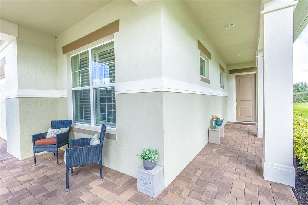 A covered front porch features a paver floor, two wicker chairs, and a tan door — 2606 MEADOWEDGE LOOP, ST CLOUD, FL