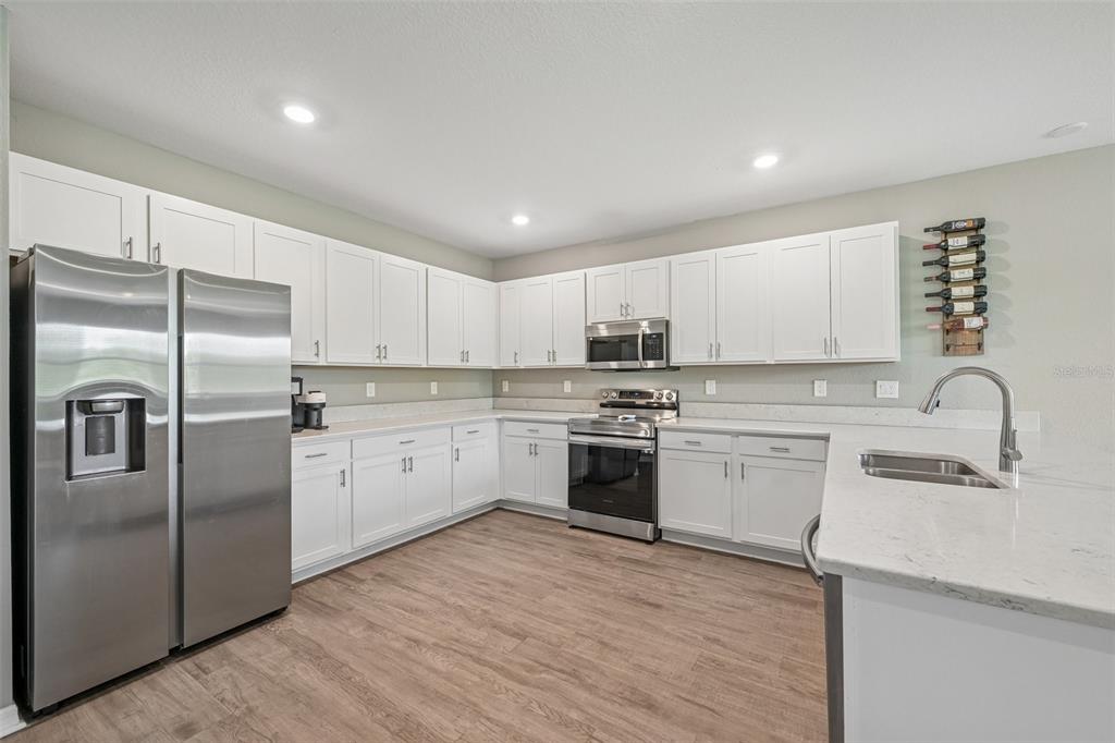 A kitchen with white cabinets, stainless steel appliances, and light countertops over wood-look flooring — 16113 67TH COURT E, PARRISH, FL