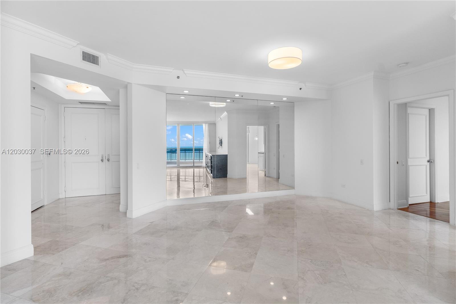 A bright, empty room features large floor tiles, a mirrored wall, and ocean views — 808 Brickell Key Dr # 3002, Miami FL 33131, MIAMI, FL