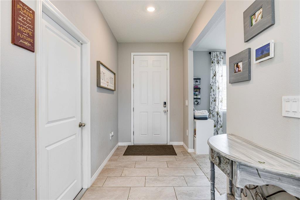 A bright entryway features light gray walls, tile flooring, a white front door, and decor — 5329 HALEWOOD COURT, BRADENTON, FL